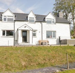A white two-story house with a black door wooden bench and hot tub in a grassy yard at Bryndan in Machynlleth