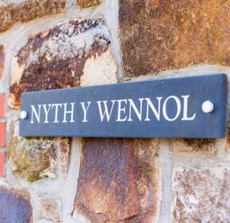 A nameplate reading NYTH Y WENNOL on a stone wall at Nyth Y Wennol in Abersoch