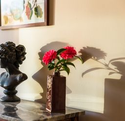 A marble top table with a dark bust sculpture and a vase with red flowers casting shadows on a wall at Nyth Y Wennol in Abersoch