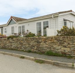 A single-story white house with a stone wall and plants along the sidewalk at 11 Pendarves in St Merryn near Padstow