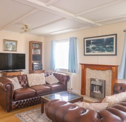 A living room with two brown leather sofas a fireplace a TV and bookshelves at 11 Pendarves St Merryn near Padstow