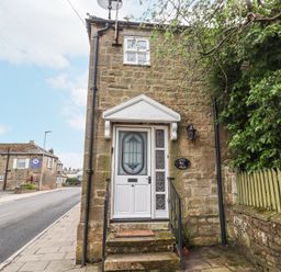 Stone house with white door and steps on a street next to a green fence with a no parking sign at Edendale in Longframlington near Alnwick