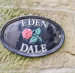 A stone wall with an oval black sign displaying a red rose and the words Eden Dale