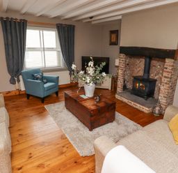 A living room with a wood burning stove a wooden chest coffee table blue armchair and beige sofas at Edendale Longframlington near Alnwick