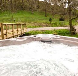 A bubbling outdoor hot tub with a wooden bridge and green trees in the background at Park Brook Retreat in Scorton