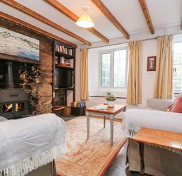 A living room with a stone fireplace two sofas a wooden coffee table bookshelf and windows at Tinners Cottage in Liskeard