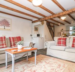 A living room with two sofas red plaid cushions a wooden coffee table and kitchen in the background at Tinners Cottage in Liskeard