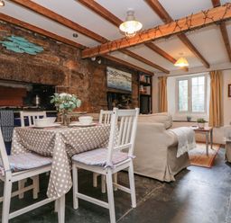 A dining area with a table and four chairs next to a living room with two sofas and a coffee table at Tinners Cottage in Liskeard