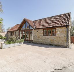A stone house with tiled roof and large glass doors with wooden frames and planted flower containers outside at The Stone Barn in Evercreech near Shepton Mallet