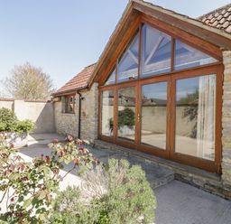 A stone building with large wooden framed glass doors and tiled roof with plants outside at The Stone Barn in Evercreech near Shepton Mallet