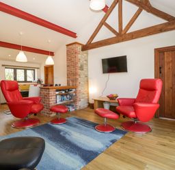 A living area with red chairs a blue rug a mounted television and exposed wooden beams at The Stone Barn in Evercreech near Shepton Mallet