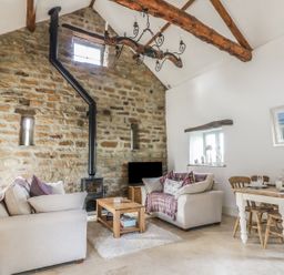 A living room with stone wall wood stove and dining table with chairs at Cottage Val in Ravenscar