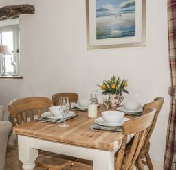 A dining table set with bowls wine glasses and a candle with wooden chairs near a window and a painting at Cottage Val in Ravenscar