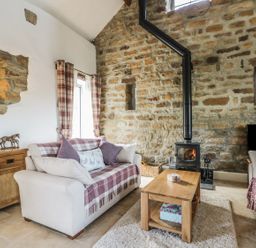 A living room with two sofas a wooden coffee table a wood-burning stove and stone walls at Cottage Val in Ravenscar