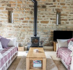 A living room with two sofas a wooden coffee table a wood burning stove and a television at Cottage Val in Ravenscar