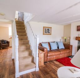 A living room with a brown leather sofa and blue cushions near a staircase at Bank House in Capel Iwan near Newcastle Emlyn
