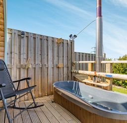 An outdoor wooden deck with a black reclining chair and a hot tub with a metal chimney at Two Hoots in Northop