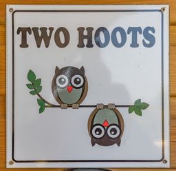A sign with two cartoon owls on a branch and the text two hoots on wood background at Two Hoots in Northop