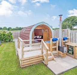 A wooden pod with a hot tub on a deck and lawn chairs on grass at Ewe Two in Oakenholt near Northop
