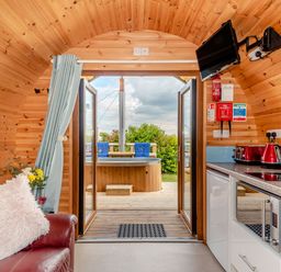 A wooden interior room with a red leather chair and kitchen appliances opening to an outdoor hot tub at Ewe Two in Oakenholt near Northop