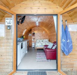 Interior of a wooden pod with double doors open showing a kitchenette a bed a red sofa and two towels hanging at Ewe Two in Oakenholt near Northop