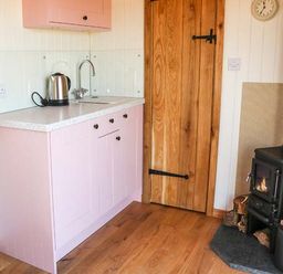 A kitchen area with a pink cabinet countertop kettle wooden door and wood-burning stove at Llety'r Bugail in Holyhead