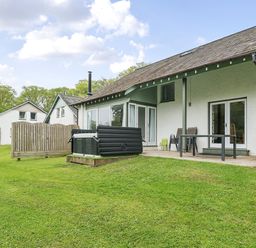 An outdoor patio with chairs and a hot tub in front of a white house with a grassy yard at Elm - Woodland Cottages in Bowness-on-Windermere