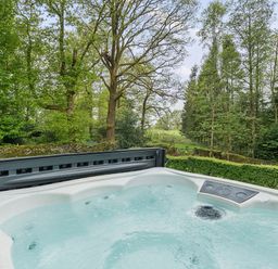 A hot tub with water in a garden area surrounded by trees and greenery at Elm - Woodland Cottages in Bowness-on-Windermere