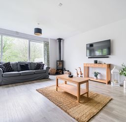 A living room with gray sofas wooden coffee table tv on wall and large windows at Elm - Woodland Cottages in Bowness-on-Windermere