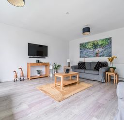 A living room with gray sofas wooden tables a wall-mounted TV and a painting at Elm - Woodland Cottages in Bowness-on-Windermere
