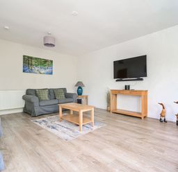 A living room with grey sofas a wooden coffee table a wall-mounted television and decorative wooden ducks at Cherry - Woodland Cottages in Bowness-in-Windermere