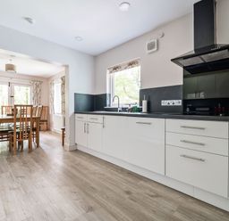 A kitchen with white cabinets a black countertop and a dining table with chairs at Cherry - Woodland Cottages in Bowness-in-Windermere