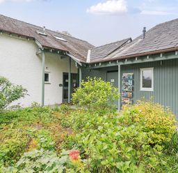 An exterior view of a building with green and white walls surrounded by plants and shrubs at Maple - Woodland Cottages in Bowness-on-Windermere