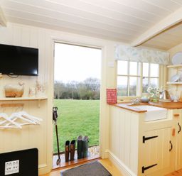 A small kitchen with wooden countertops and a sink next to an open door showing a grassy field at Bramble Burlawn near Wadebridge