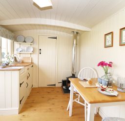 A small kitchen with wooden countertops a wood stove a table with food and flowers at Bramble Burlawn near Wadebridge