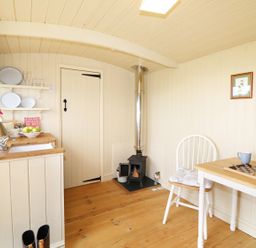 A small kitchen area with a wood stove a table and chair with a game board and flowers at Willow Burlawn near Wadebridge