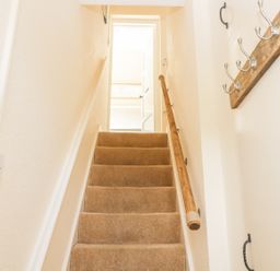 A carpeted staircase with wooden handrails leading to an open door at Oak Lodge in East Runton