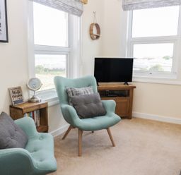A living room with two armchairs a small wooden side table a television on a wooden stand and windows at Oak Lodge in East Runton