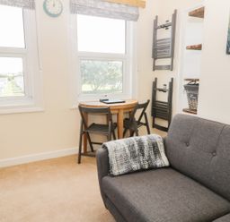 A small living room with a gray sofa a round wooden table with two chairs and two windows at Oak Lodge in East Runton