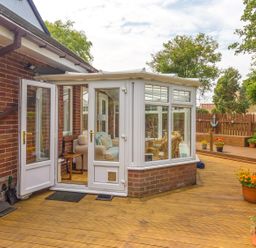 A wooden deck leading to a conservatory with open doors and potted plants on the side at Estuary View in Warkworth