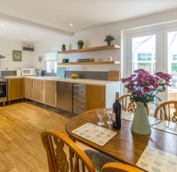 A kitchen with wooden cabinets a dining table with flowers and wine near glass doors at Estuary View in Warkworth