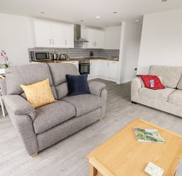 A living room with two sofas a wooden coffee table and a kitchen with white cabinets in the background at Beechnut Cottage in Tewkesbury