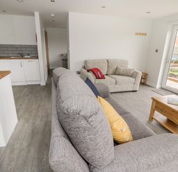 A living room with two sofas a wooden coffee table and a kitchen area at Beechnut Cottage in Tewkesbury