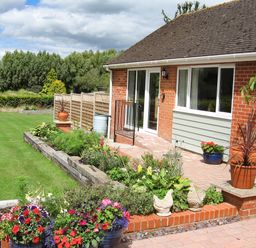 Front garden with plants and flowers along a brick house with sliding doors at Beechnut Cottage in Tewkesbury