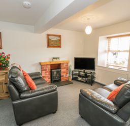 A living room with two black leather sofas a wooden cabinet a TV on a stand and a brick fireplace at Brickfield Cottage in Machynlleth