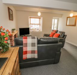A living room with black leather sofas a wooden cabinet with flowers a small TV and a window at Brickfield Cottage in Machynlleth