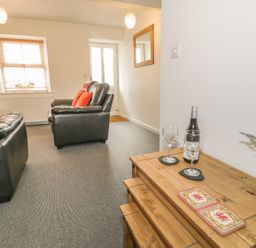 A living room with black leather sofas a bottle of wine and two wine glasses on a wooden table at Brickfield Cottage in Machynlleth