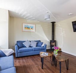 A living room with blue sofas a wood stove a wall mounted TV and nesting tables at Rocky Close in St Ives