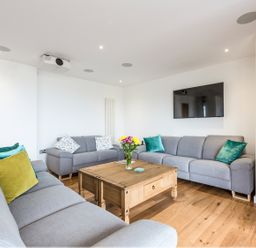 A living room with three gray sofas a wooden coffee table with flowers and a mounted television at Chy Lowen in St Ives