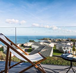 A deck chair and table with wine glasses overlooking a coastal holiday park at Chy Lowen in St Ives